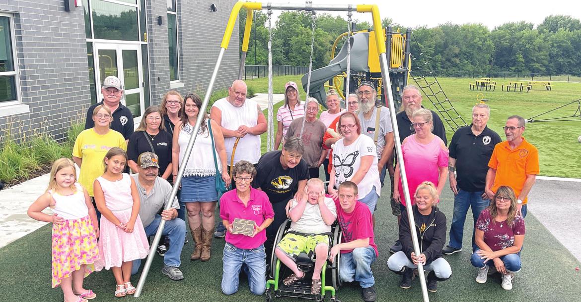 DIANA REINERT (kneeling, pink shirt), Cheryl Mick (behind Reinert) and members of the Excelsior Springs Fraternal Order of Eagles donate a wheelchairaccessible, adaptive swing to Cornerstone Elementary. Trying out the swing is Bently Ford, 10, with father Travis Ford and mother Sarah Loveall beside him. BRIAN RICE | Staff